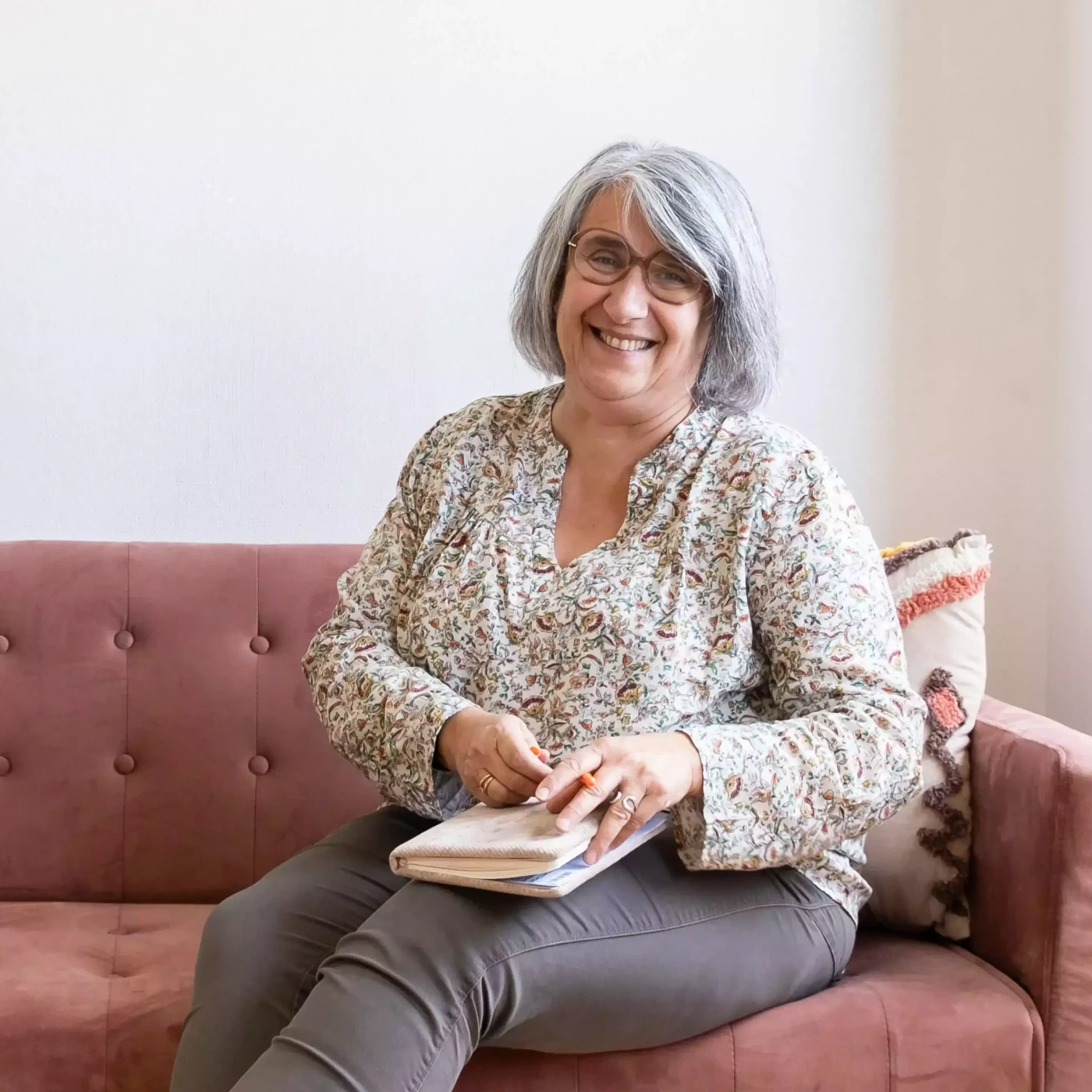 Sandra BLACHE, sophrologue à Lyon, assise sur le canapé de son cabinet, un carnet sur les genoux
